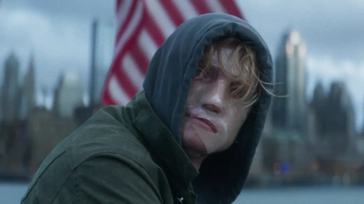 Tom Rhys Harries como Matt Hagen, de capuz, com o rosto marcado e prédios de Gotham ao fundo