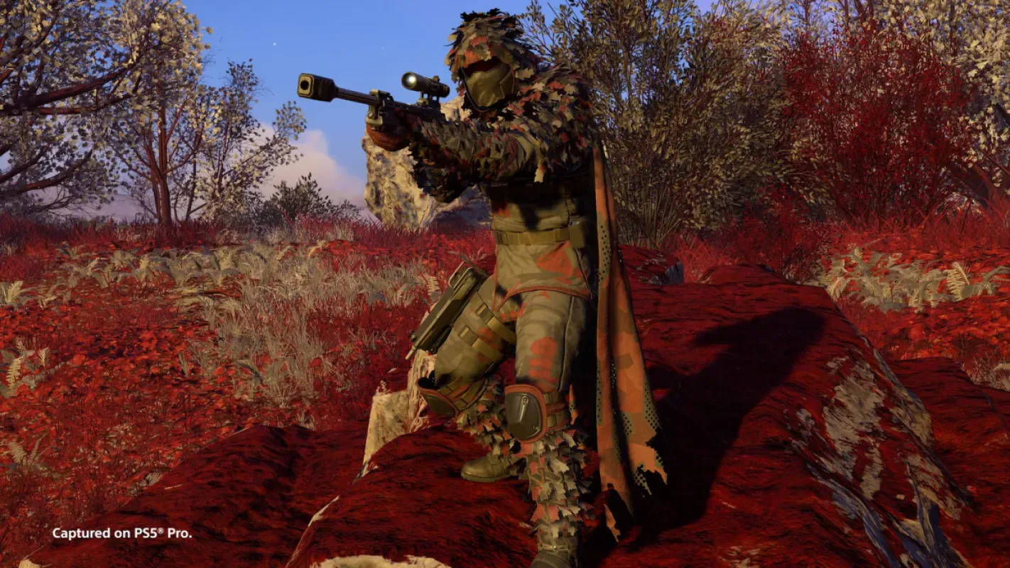 Helldiver com armadura de camuflagem ghillie aponta um fuzil de precisão em vegetação vermelha