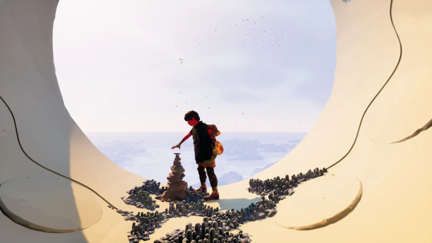 Personagem com mochila toca uma pilha de pedras dentro de uma abertura circular em formações de areia, com o mar ao fundo, em cena de Jusant