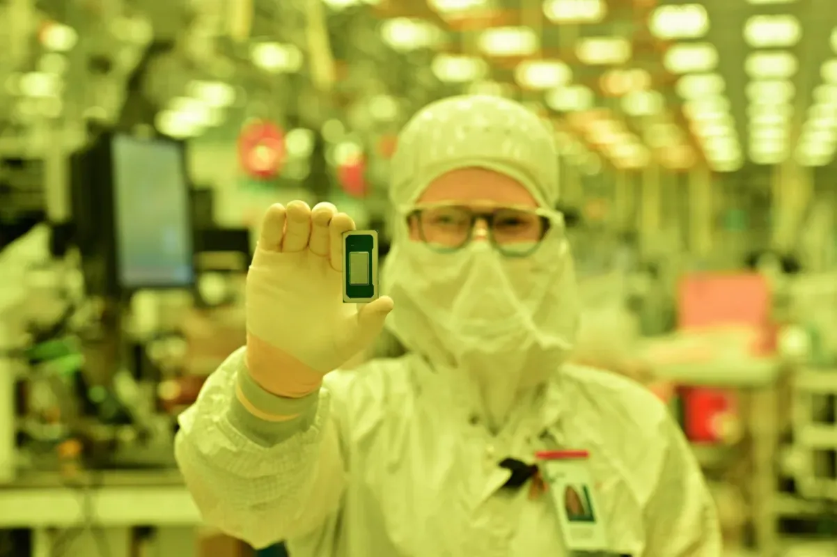 Técnico da Intel com traje de sala limpa e óculos ergue um processador Intel Core Ultra série 3, fabricado no processo 18A, em uma fábrica iluminada por luz amarela
