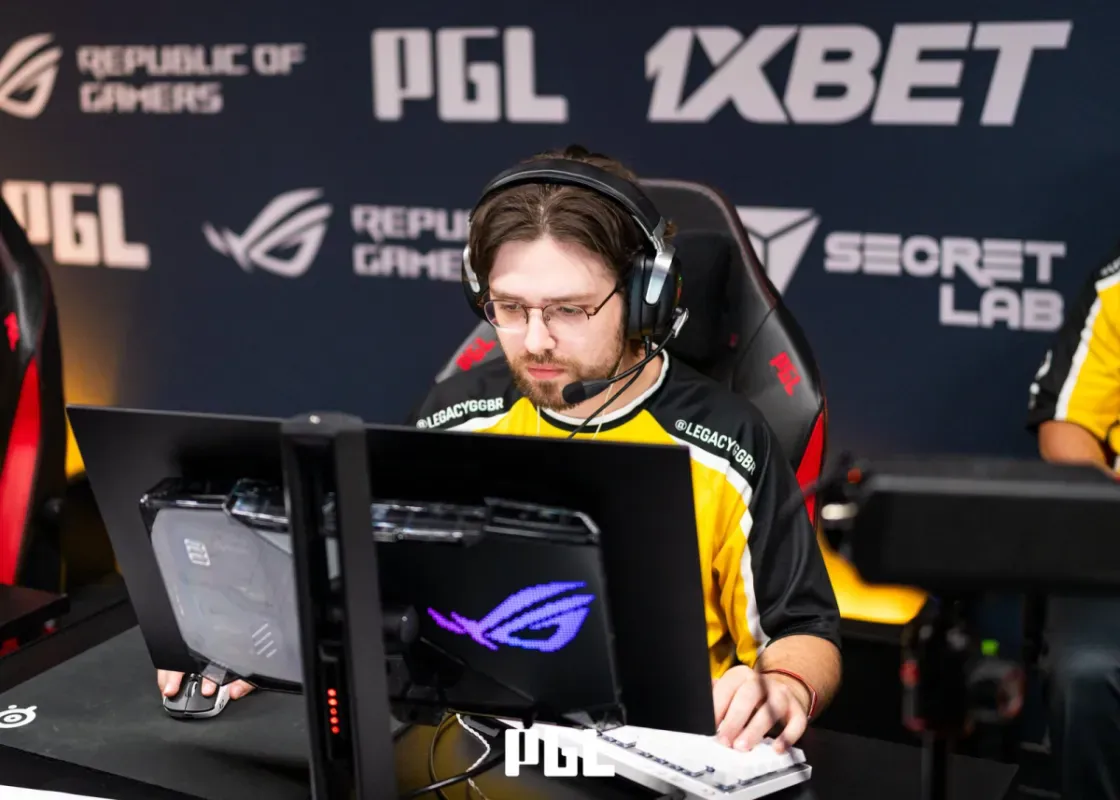 Jogador da Legacy de fone de ouvido e camisa amarela e preta, sentado diante do monitor no palco da PGL Masters Bucharest
