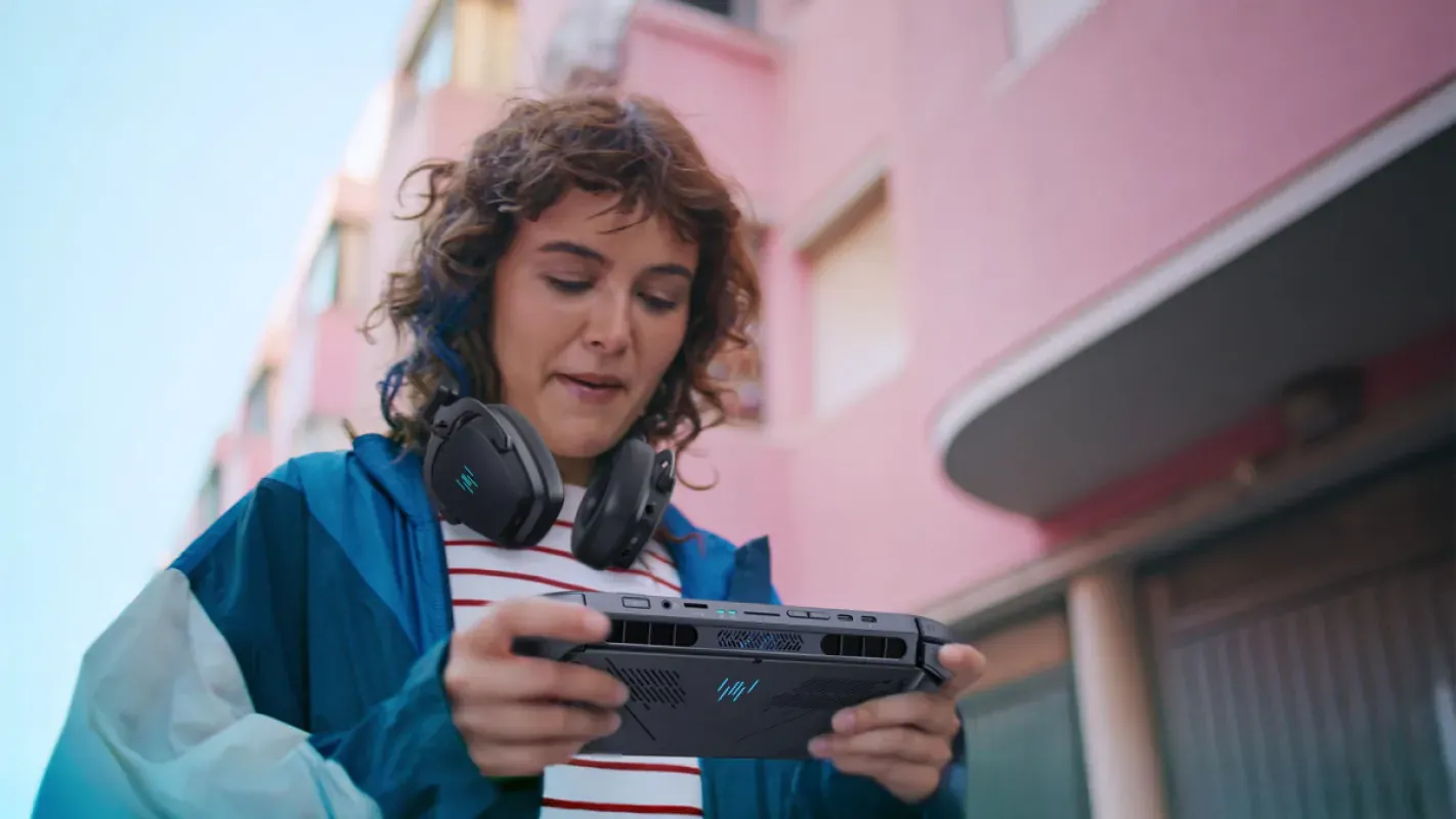 Jovem com fones no pescoço joga no Acer Predator Atlas 8 em uma rua
