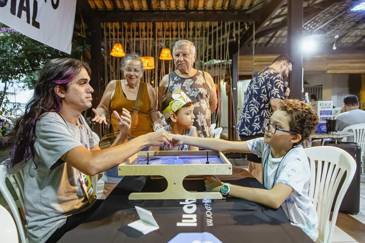 Criança e adultos disputam partida de jogo de mesa em edição anterior do Mesa Fest