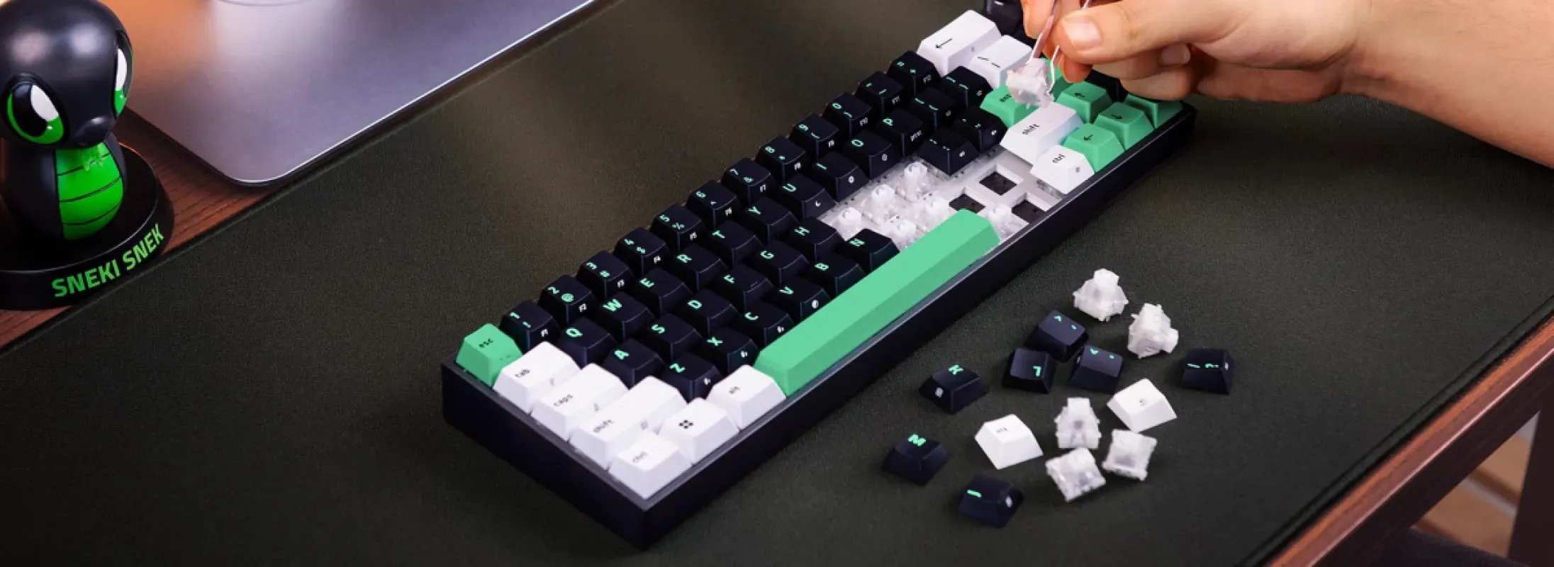 Pessoa troca switches do teclado Razer Reclusa Mini 65% com teclas pretas, brancas e verdes sobre uma mesa